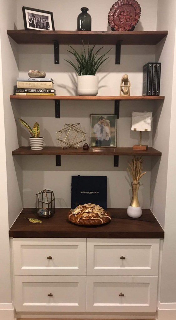 A shelving unit with a dark wood top and white base, featuring three shelves with various decorative items, including book...